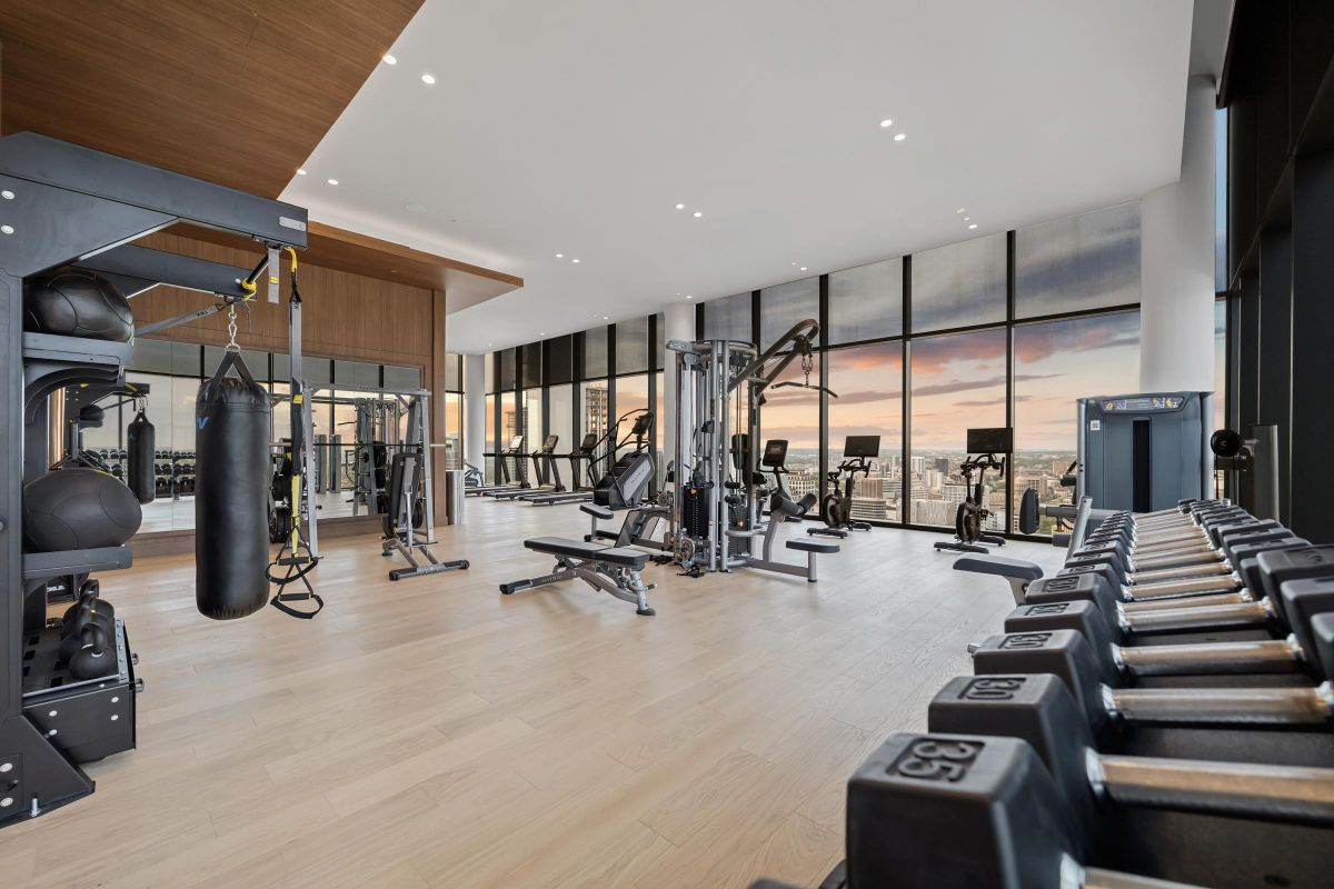 Modern gym with exercise machines, weights, and a punching bag, featuring large windows with a cityscape view.
