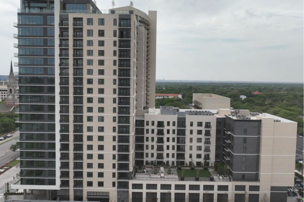A modern multi-story apartment building with large windows and balconies, surrounded by trees and roads.