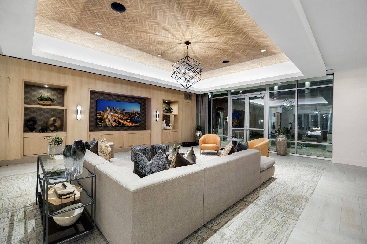 Modern living room with beige sectional sofa, glass coffee table, wall-mounted TV, and decorative ceiling lights.