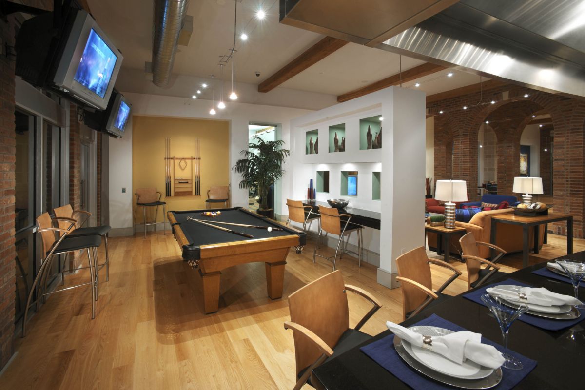 Modern loft with a pool table, dining area, and lounge, featuring wood floors and exposed brick walls.