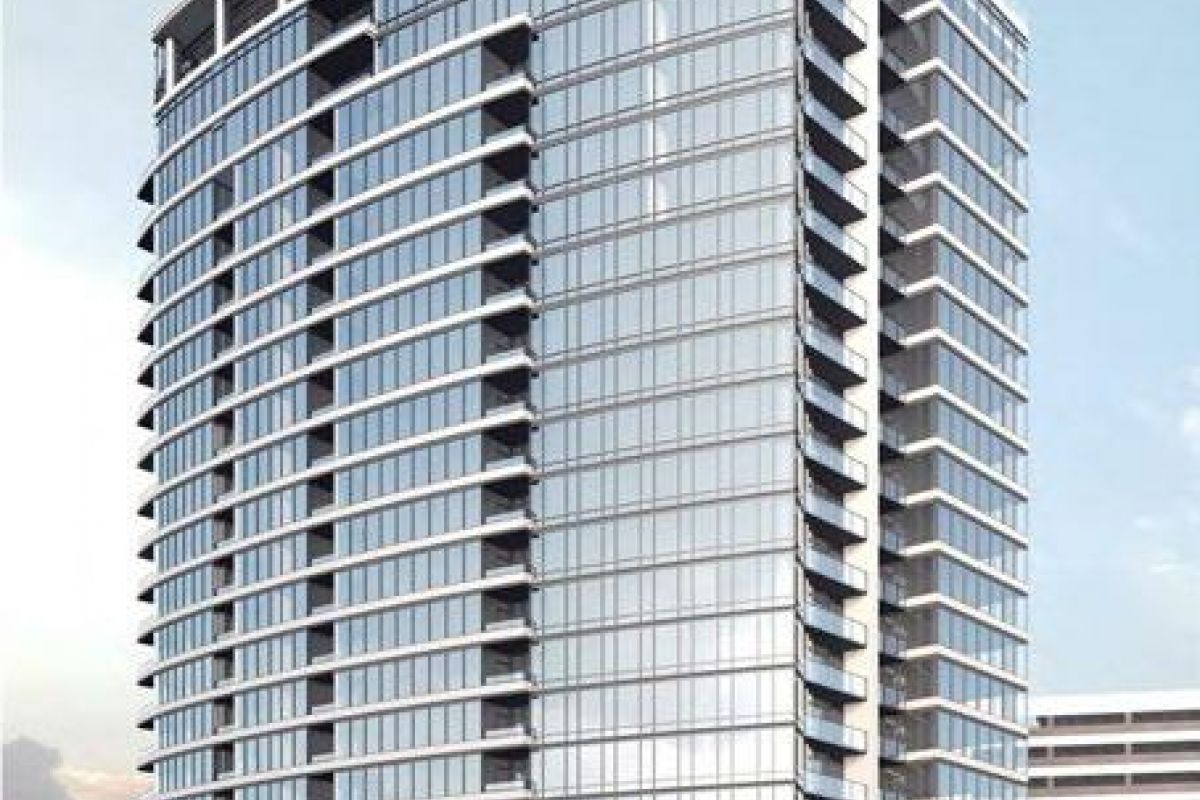 Tall modern glass building with balconies, surrounded by a clear sky and small green trees at the base.
