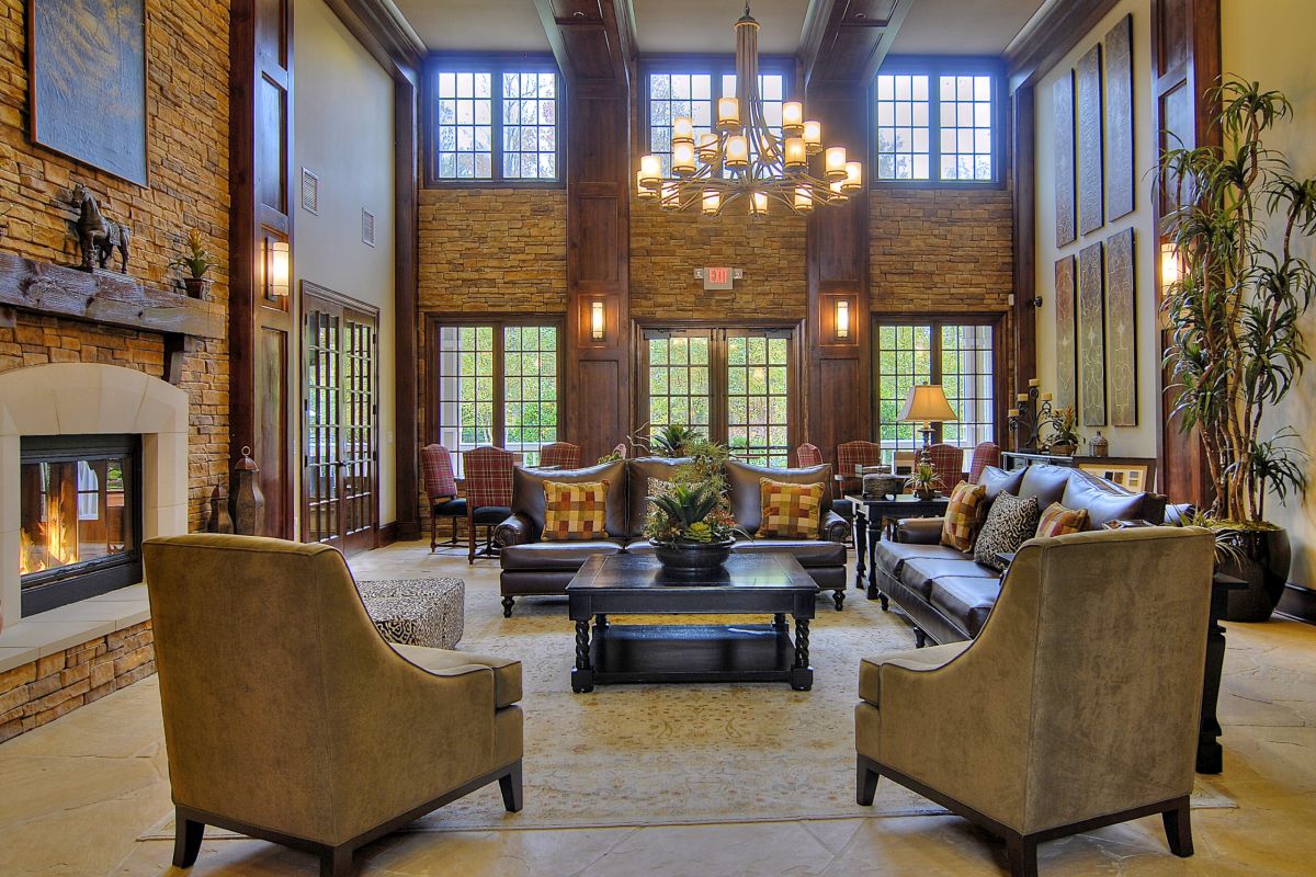 Elegant, spacious living room with stone fireplace, large windows, chandelier, and comfortable seating.
