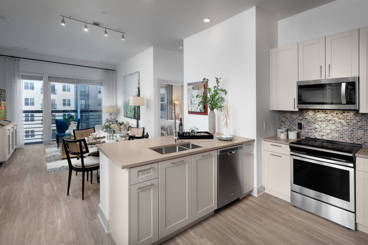 Modern open-plan kitchen and living area at Hanover Mystic River, featuring light wood floors, white cabinets, and stainless steel appliances.