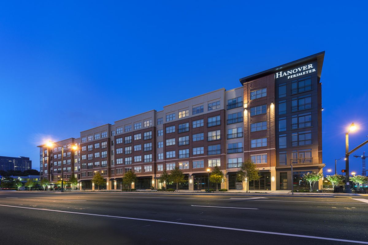 A modern apartment building, Hanover Perimeter, is lit up at dusk beside an empty street.