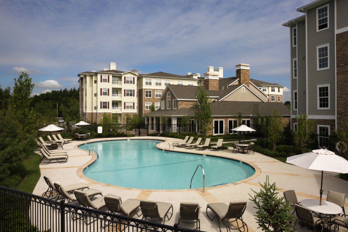 Large outdoor pool surrounded by lounge chairs and umbrellas, with apartment buildings in the background.