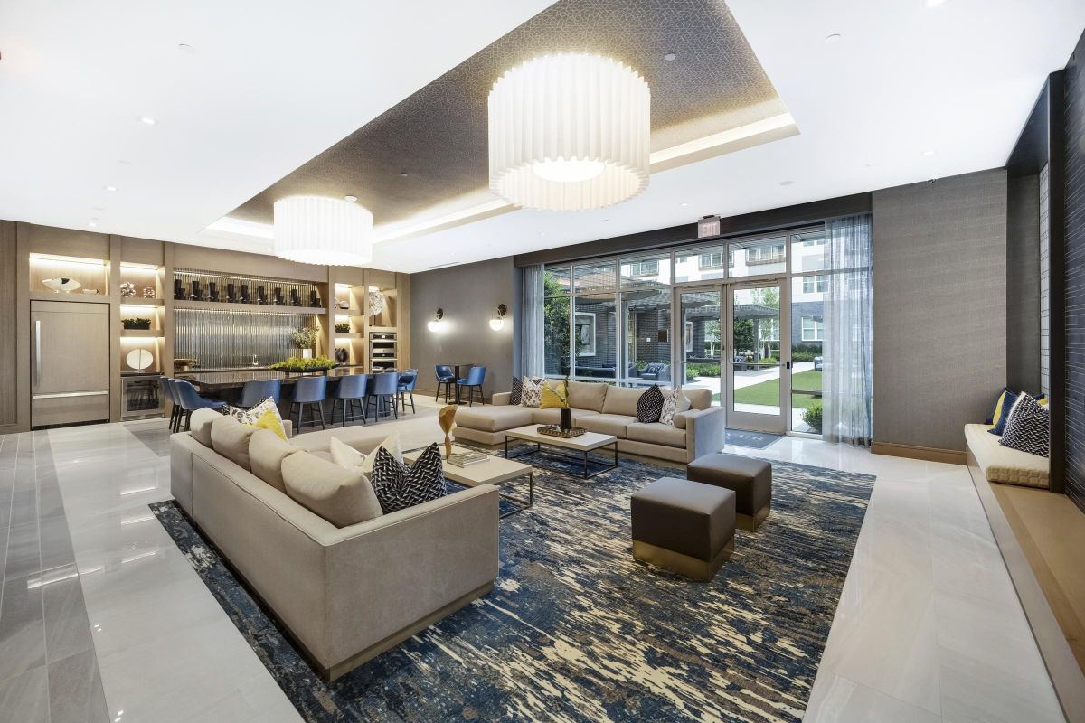 Modern lounge with sofas, blue patterned rug, dining table, and large windows overlooking a green space.