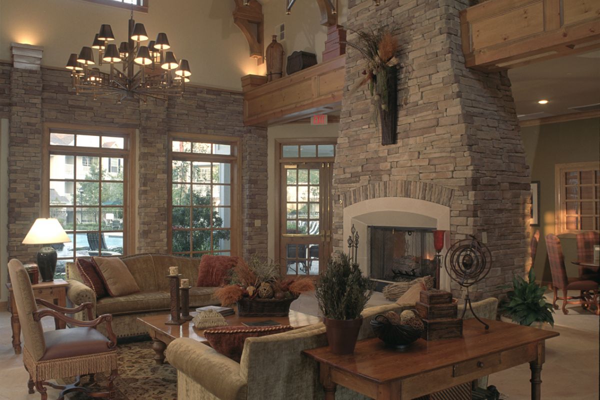 Spacious living room with tall stone fireplace, large windows, chandeliers, and cozy, traditional furniture.