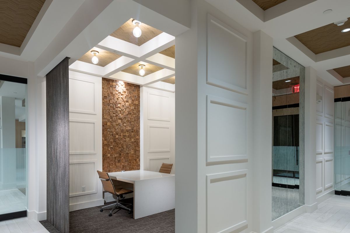 Modern office space with a desk, two chairs, wood accent wall, and bright overhead lighting.
