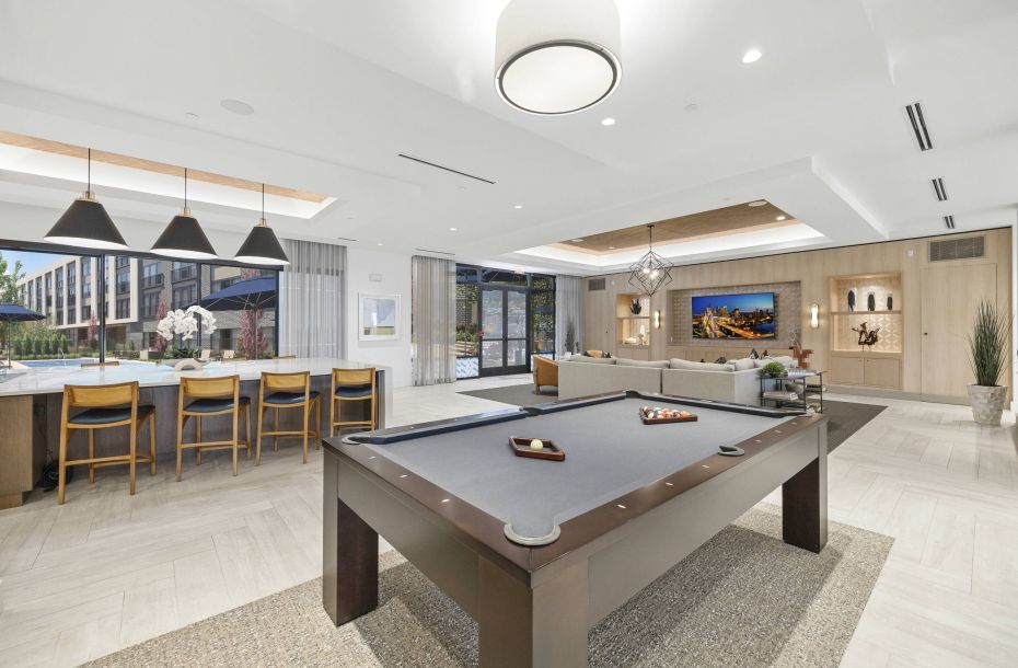 Hanover Company, Hanover Crossing Residences Modern game room with a pool table, bar seating, and large TV in a spacious, well-lit area.