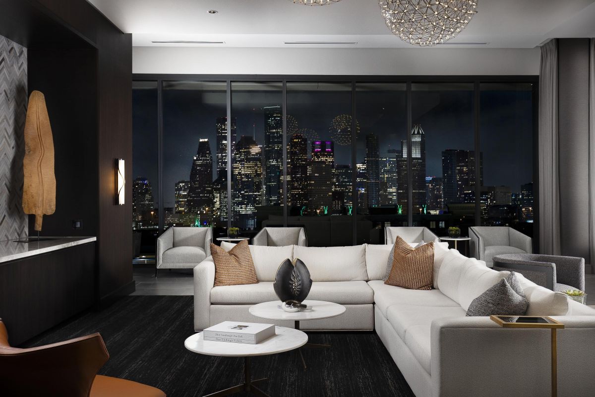Luxurious modern living room with white sofas, city skyline view through large windows, and elegant lighting fixtures.
