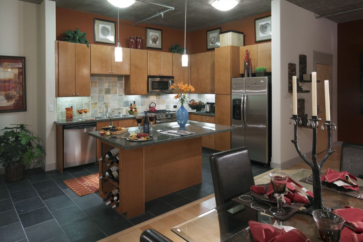 Modern kitchen with wood cabinets, stainless steel appliances, island, and set dining table with red napkins.