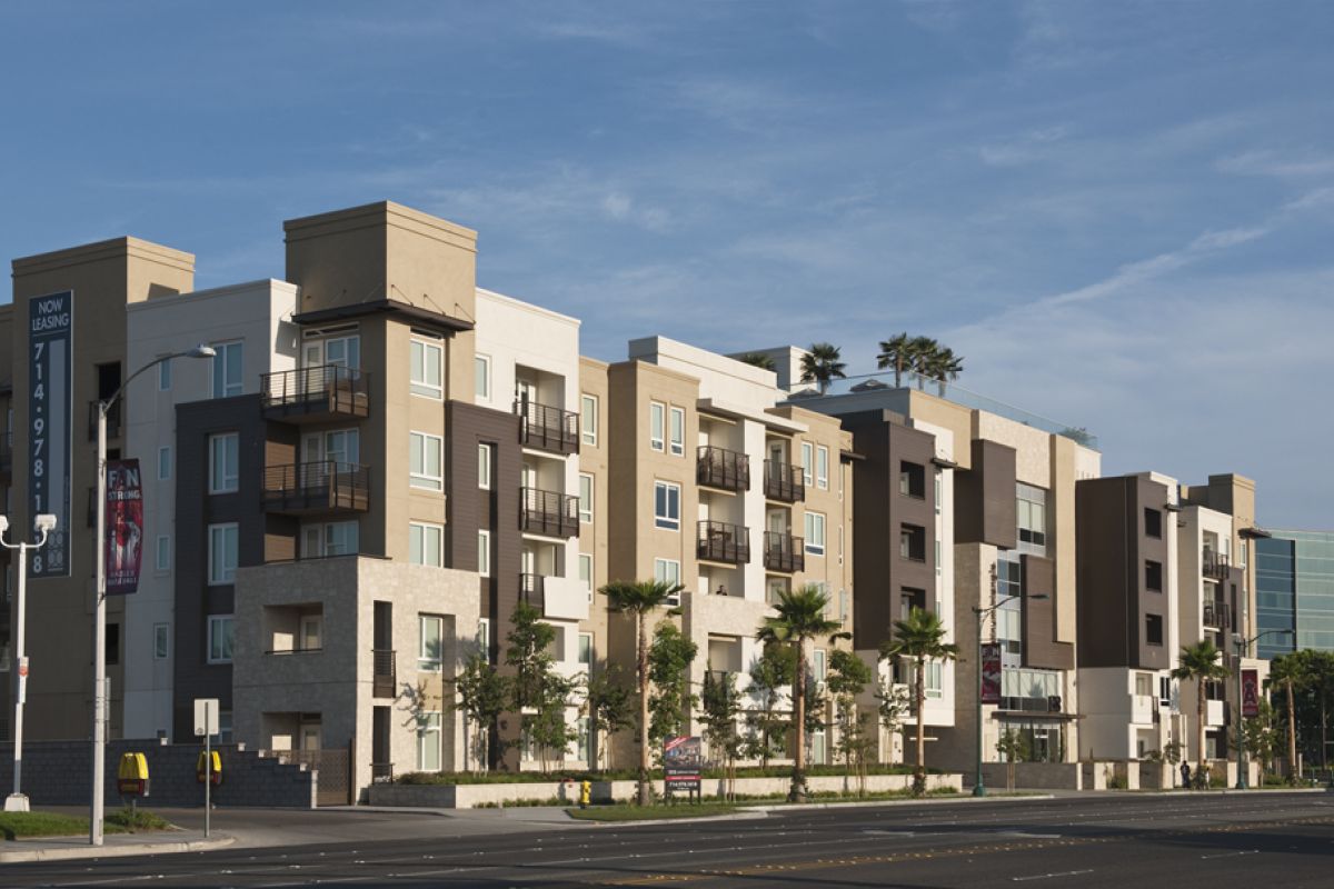 Modern, multi-story apartment building with balconies, palm trees, and a clear blue sky in the background.