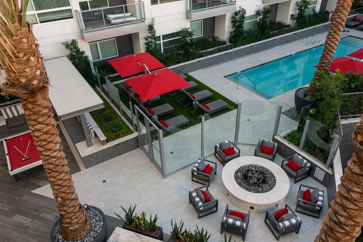Modern Hanover Diridon apartment courtyard with a pool, red umbrellas, lounge chairs, and a fire pit seating area.