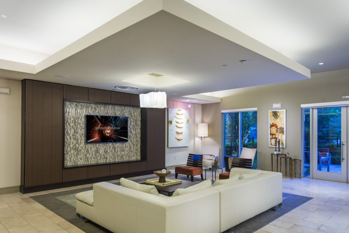 Modern lounge with a white sectional sofa, TV on a feature wall, and large windows overlooking greenery.
