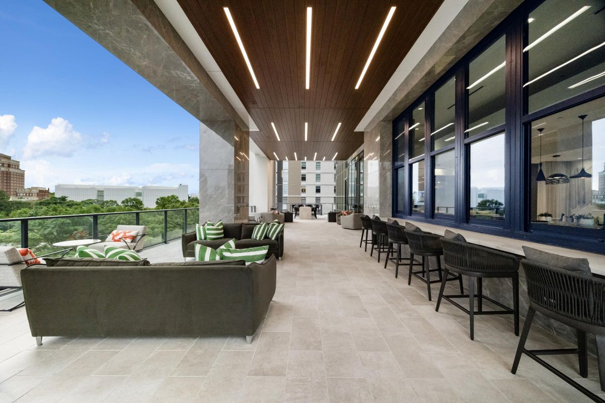 Rooftop patio with modern seating, a long bar, and city views under a wooden ceiling with sleek lighting.