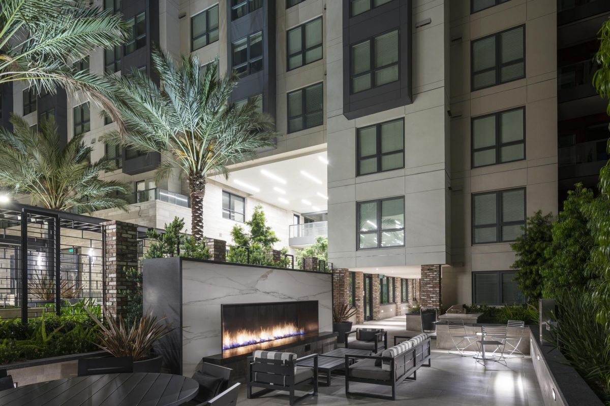 Modern apartment courtyard at night with a fire pit, tables, and seating, surrounded by palm trees.