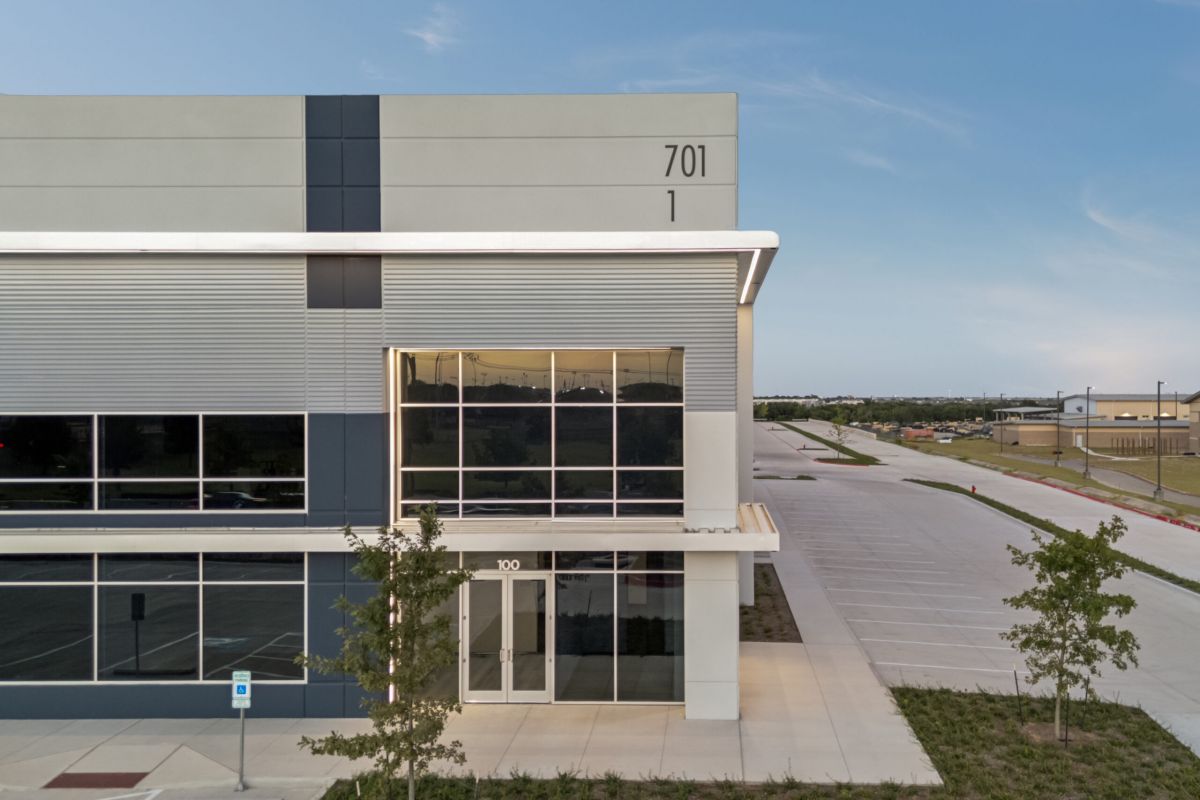 Modern commercial building with large windows, labeled 701, next to an empty parking lot and clear sky.