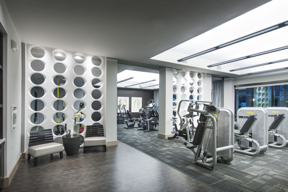 Modern gym with exercise machines, cardio equipment, and seating area with chairs and a potted plant.