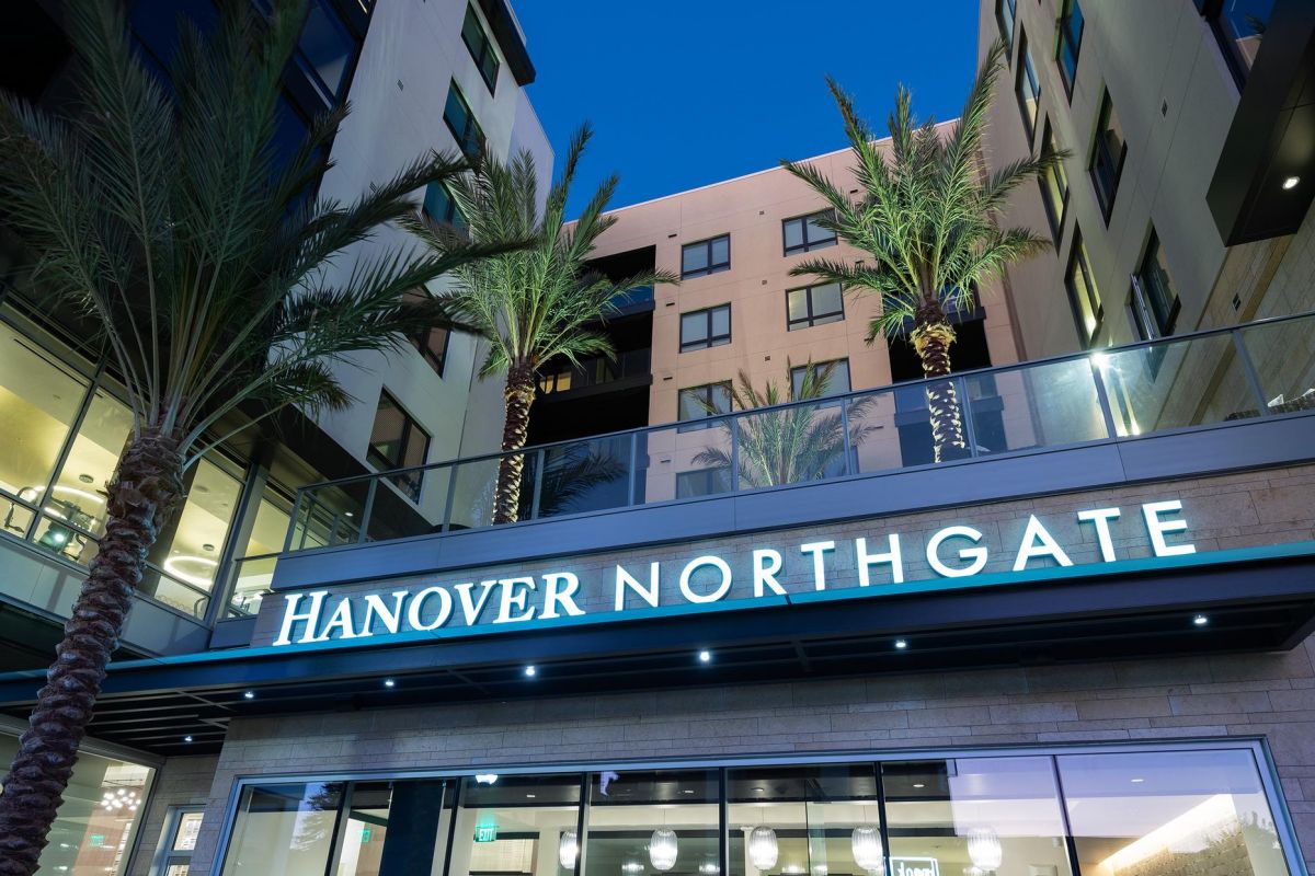Modern apartment building with palm trees and a lit "Hanover Northgate" sign at dusk.