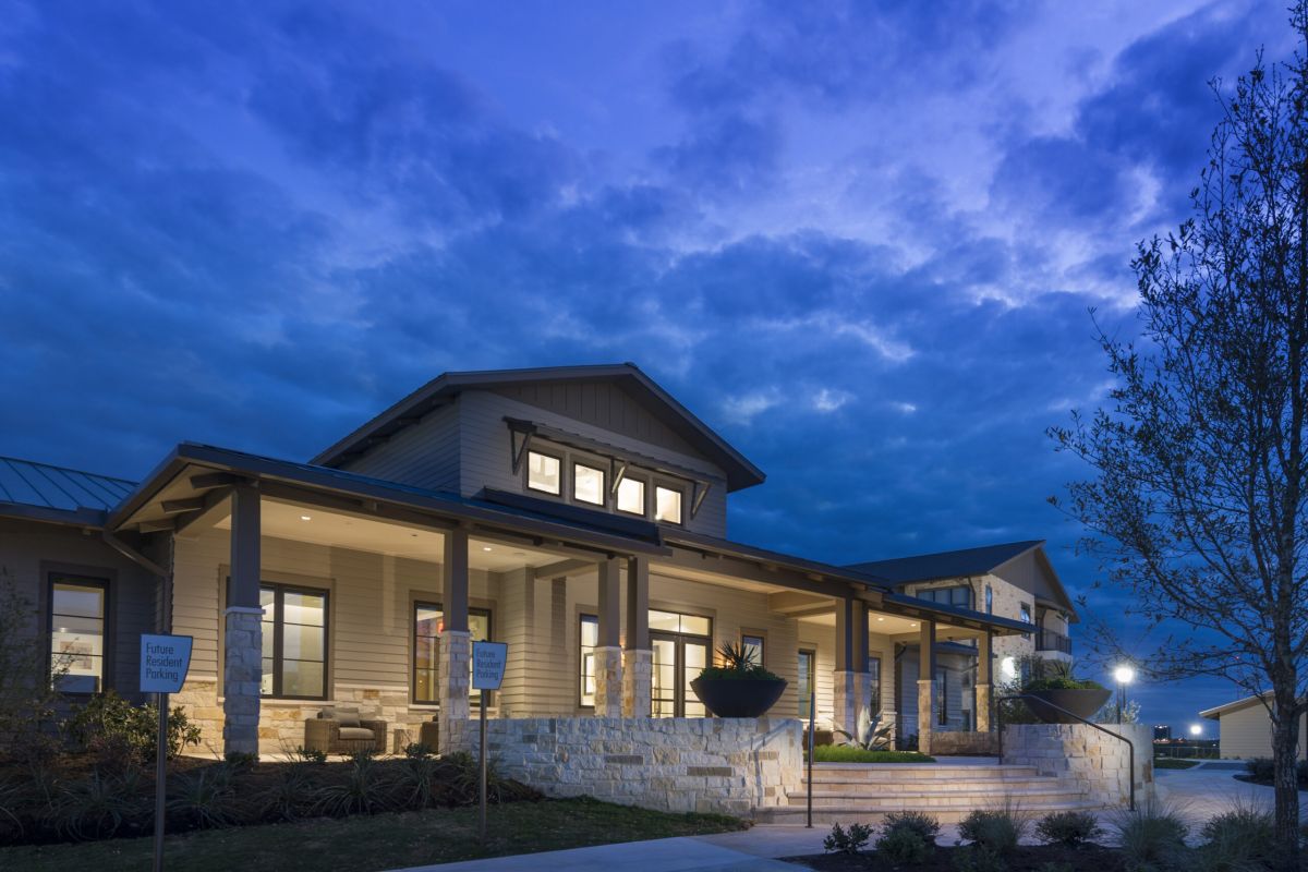 A modern house with large windows and a lit porch at dusk under a dramatic, cloudy blue sky.