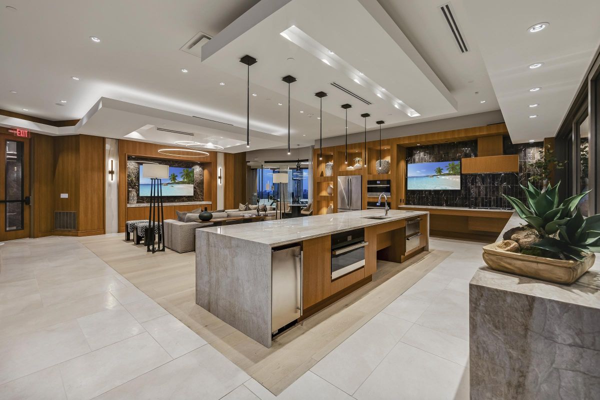 Modern open-concept kitchen with an island, pendant lights, and wood accents, leading to a living area.