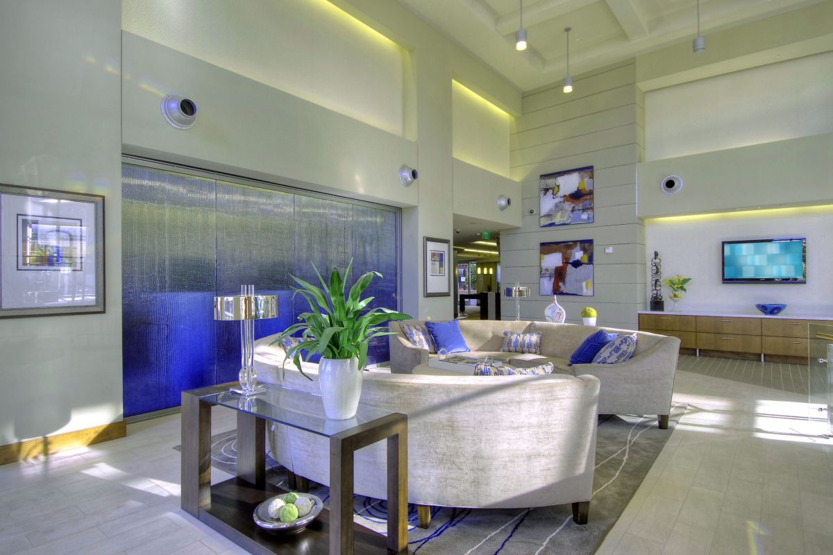 Modern lobby with curved sofas, a water feature, wall art, plants, and a TV in a bright, spacious room.