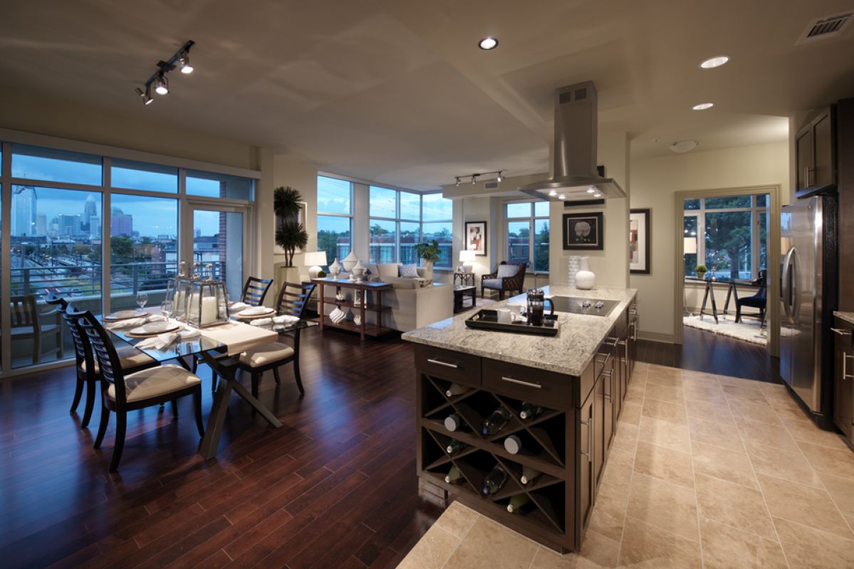 Modern open-concept kitchen, dining, and living area with large windows and city views at dusk.