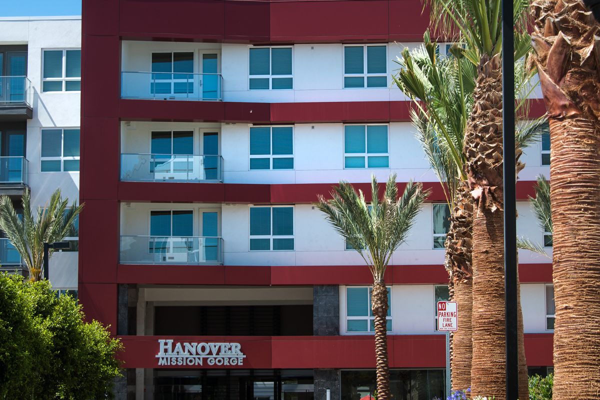 Modern apartment building with red accents, palm trees, and a clear blue sky.