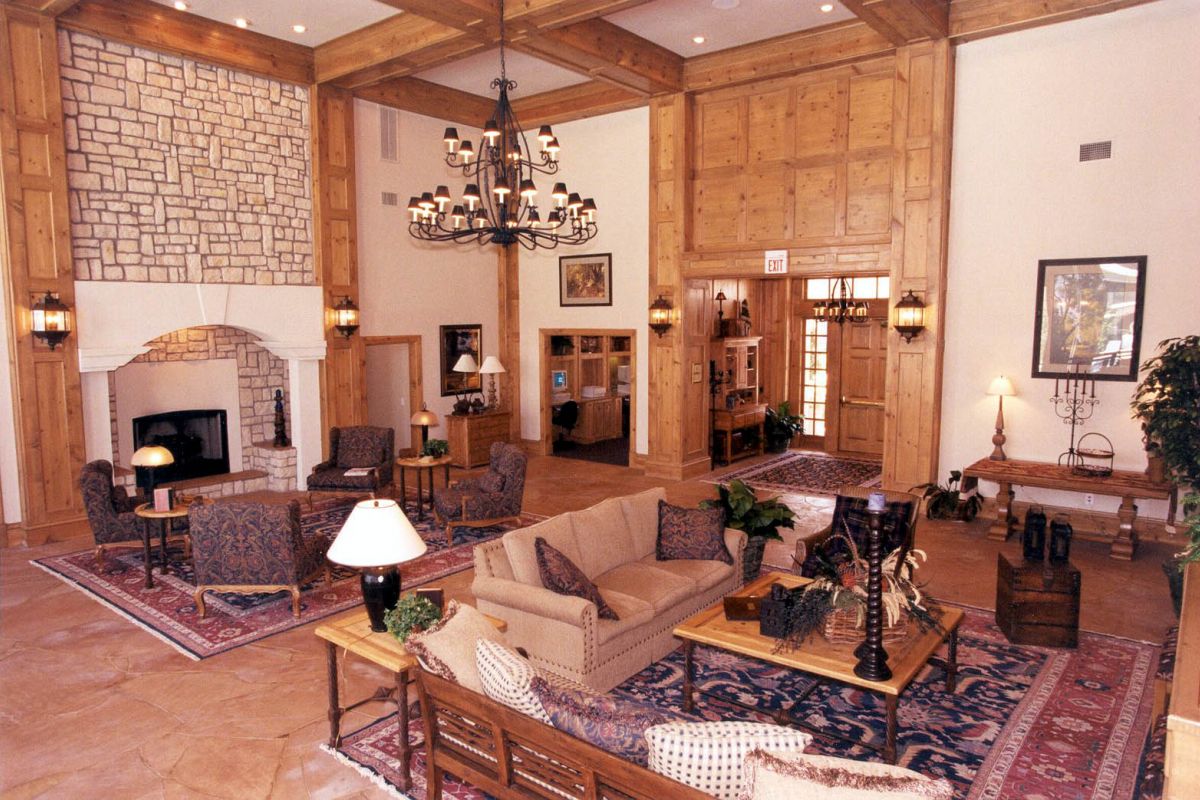 Spacious, elegant living room with a fireplace, chandeliers, and wooden accents—experience refined Dallas apartments at Churchill on the Park.