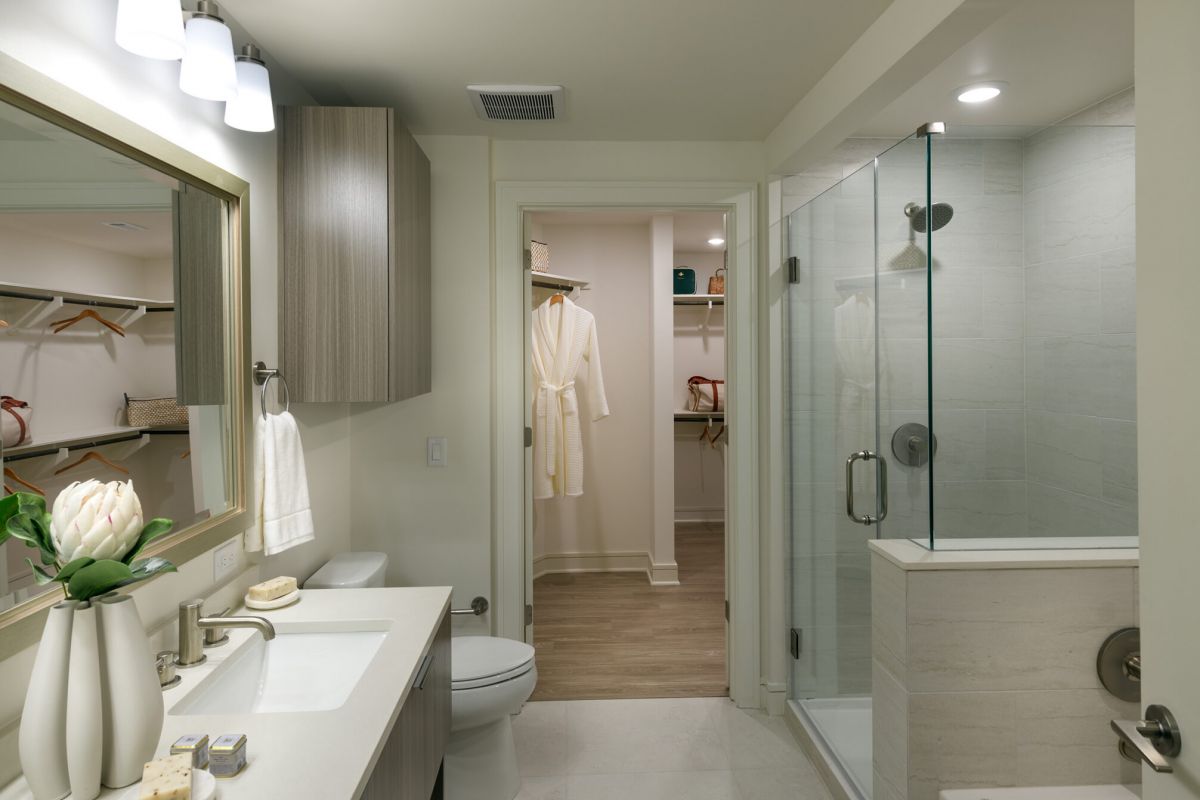Modern bathroom in Hanover apartments features double sinks, glass shower, and walk-in closet overlooking Buffalo Bayou.