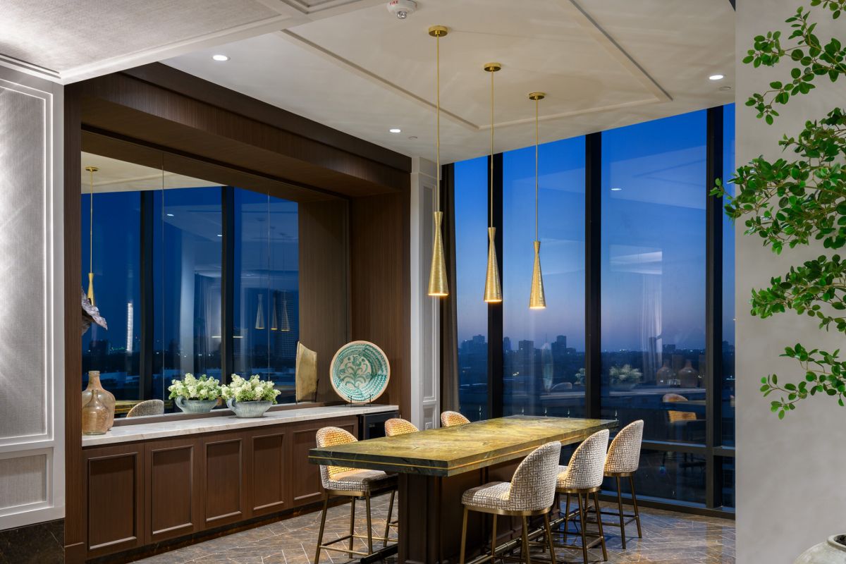 Modern dining area with marble floors, gold pendant lights, and Buffalo Bayou views through floor-to-ceiling windows at dusk.