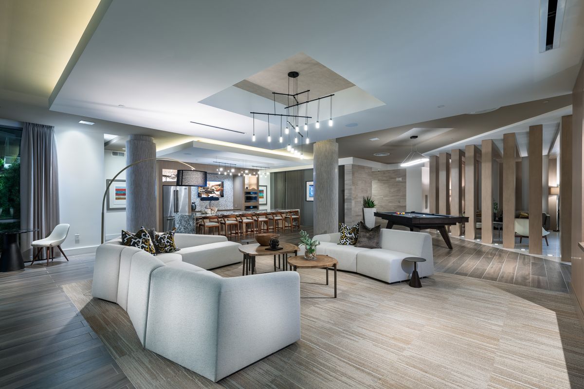 Modern lounge with white sofas, kitchen area, pool table, and contemporary lighting and decor.