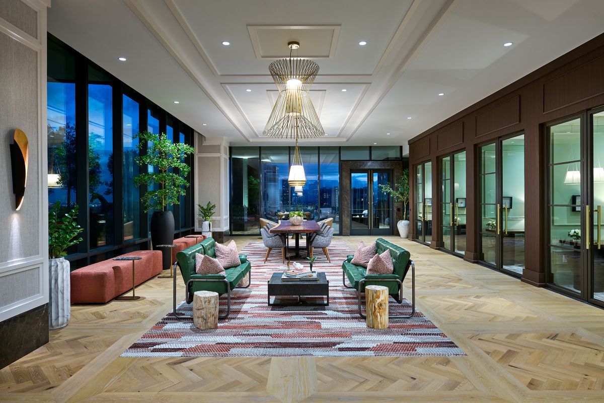 Modern lounge at Hanover with green chairs, patterned rug, large windows, wood floors, and views near Buffalo Bayou.