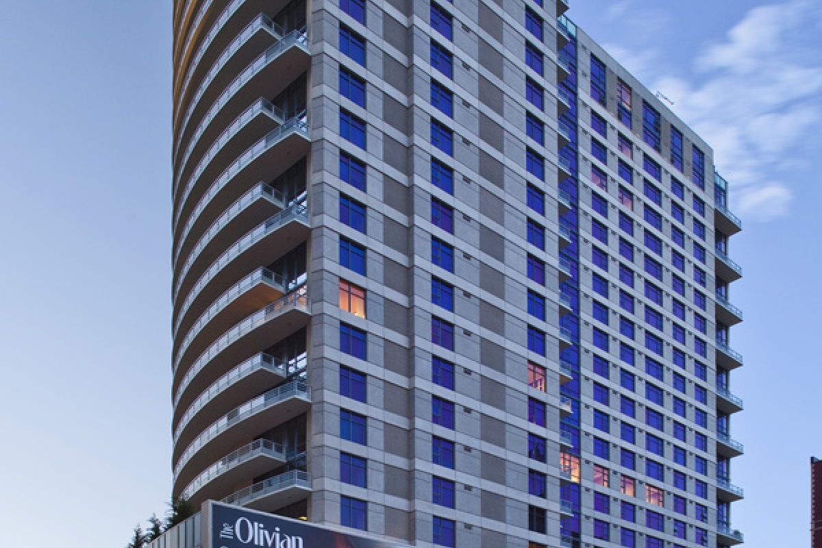Tall modern apartment building with balconies and blue windows, photographed at dusk from street level.