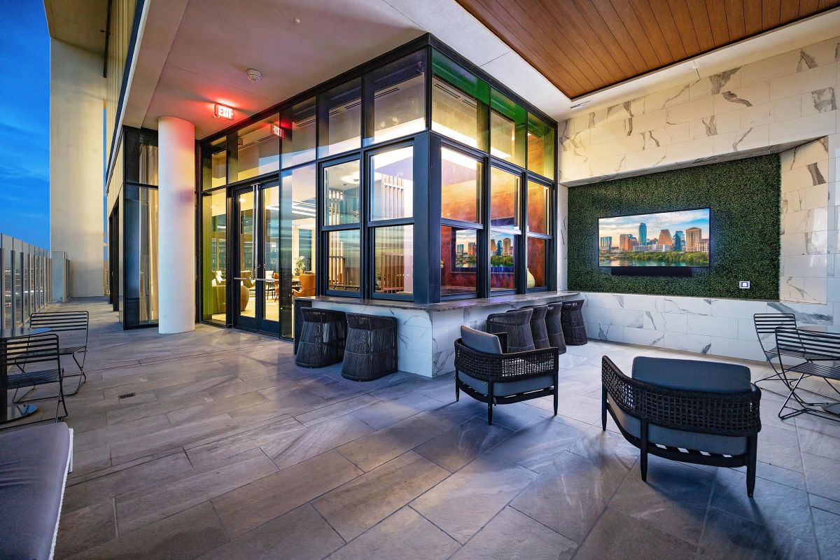 Modern outdoor patio with seating, large windows, and cityscape artwork on the wall in evening light.