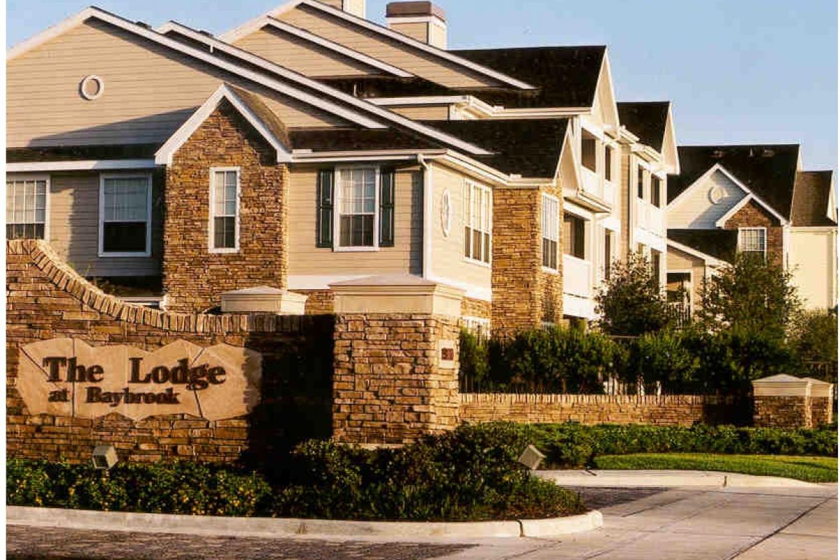 A modern apartment complex with stone exterior near Broadwater Galveston, featuring a sign reading "The Lodge at Baybrook" at the entrance.