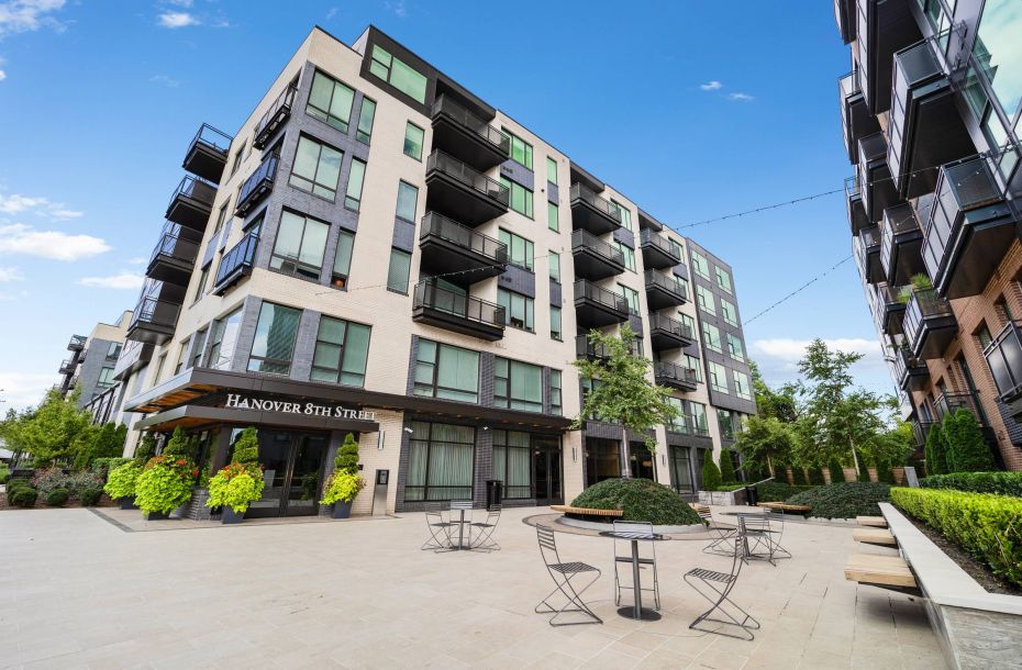 Hanover Company, Hanover 8th Street Modern apartment building with balconies and outdoor seating area under a clear blue sky.
