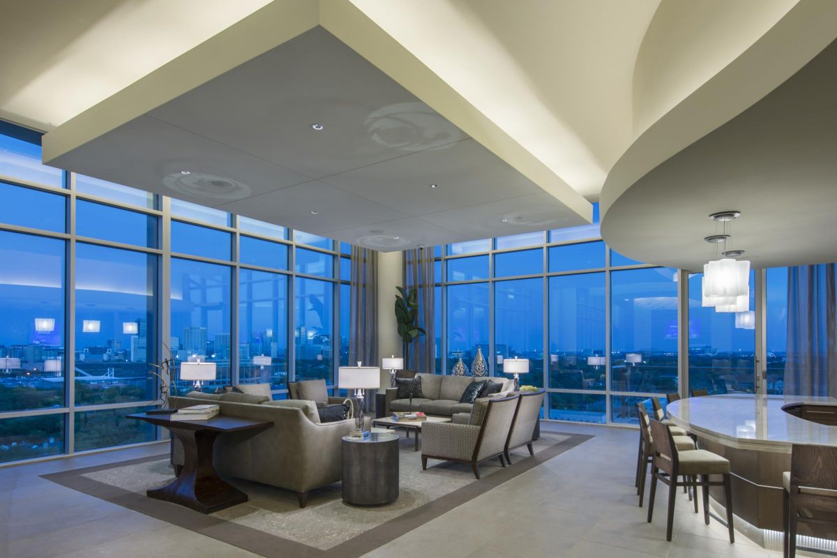 Luxurious modern living room with large windows, plush sofas, a chandelier, and city skyline view at dusk.