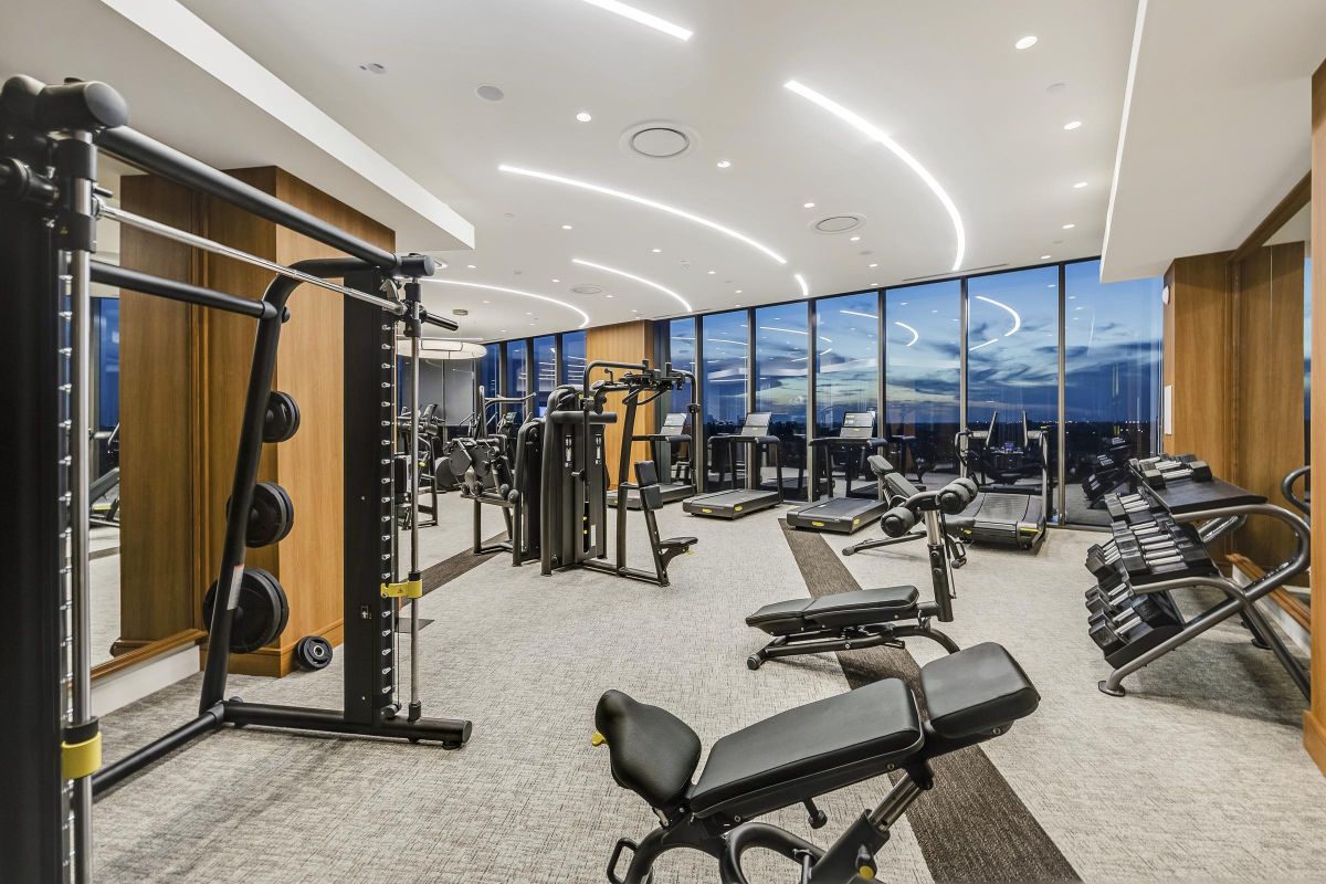 Modern gym with various exercise equipment and large windows overlooking a cityscape at dusk.