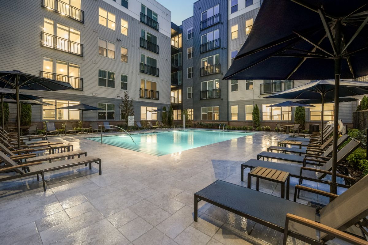 Modern Stoneham apartment pool courtyard at dusk with lounge chairs, umbrellas, and multi-story Hanover buildings surrounding the space.