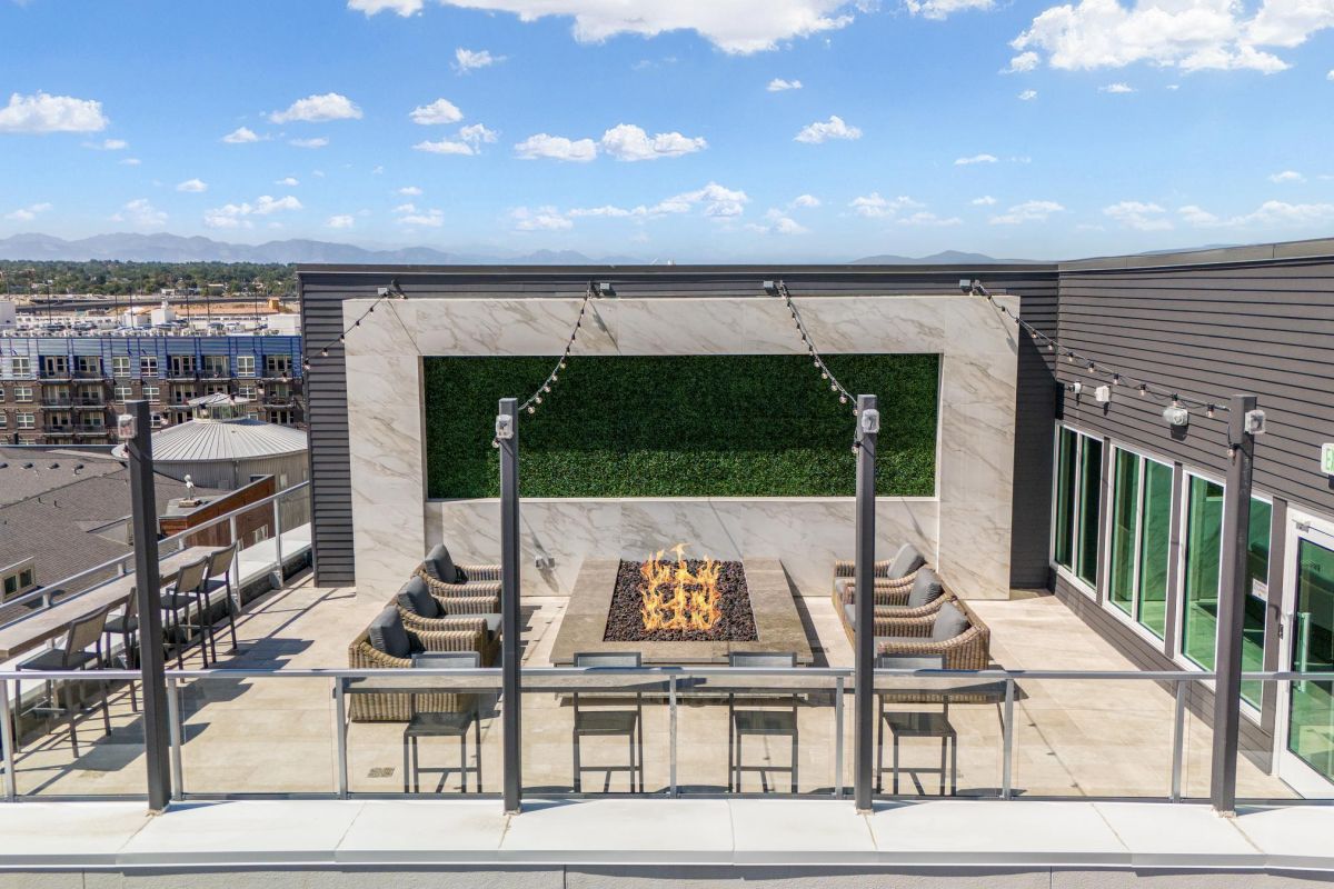 Rooftop patio with a fire pit, surrounded by chairs and tables, overlooking distant mountains and cityscape.