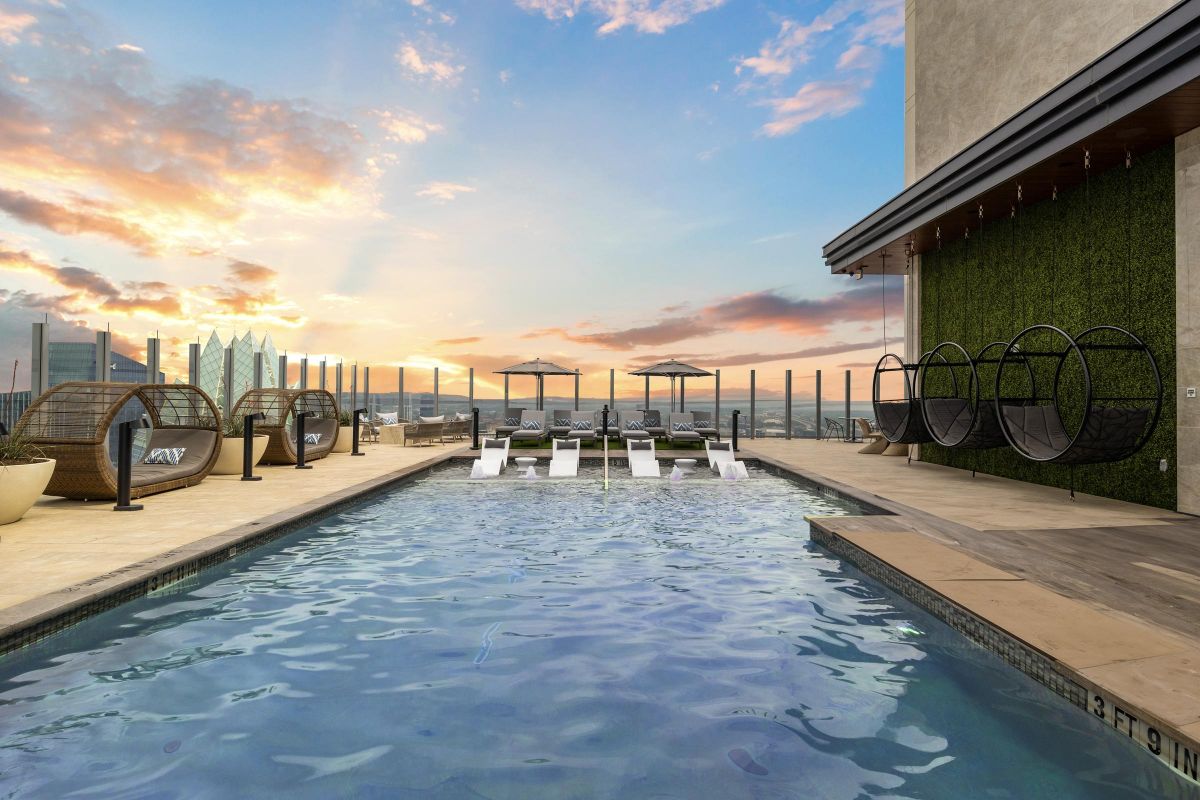 Rooftop pool with lounge chairs, hanging chairs, and a city view at sunset.