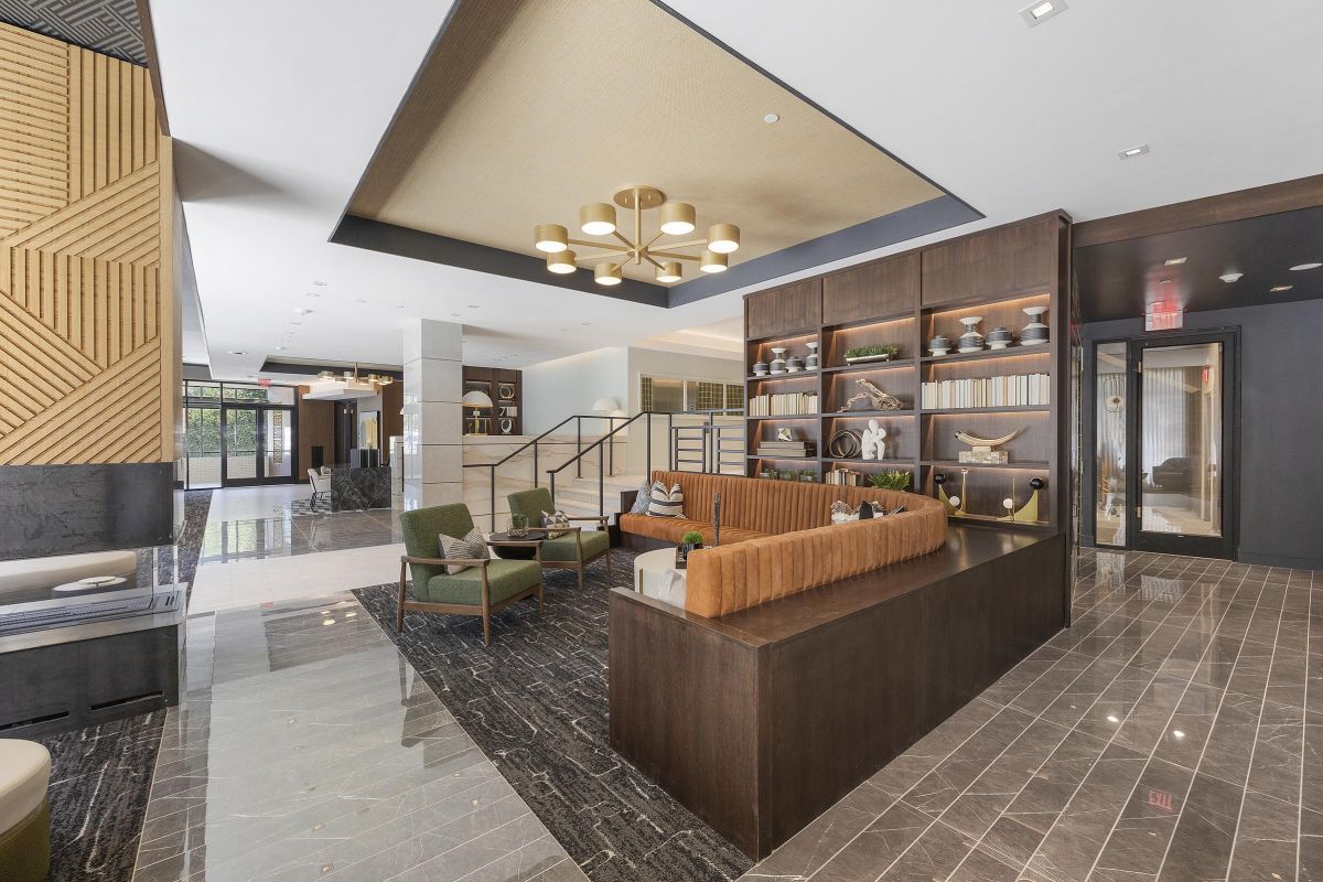 Modern hotel lobby with seating area, wooden partitions, and decorative shelves under a geometric ceiling light.