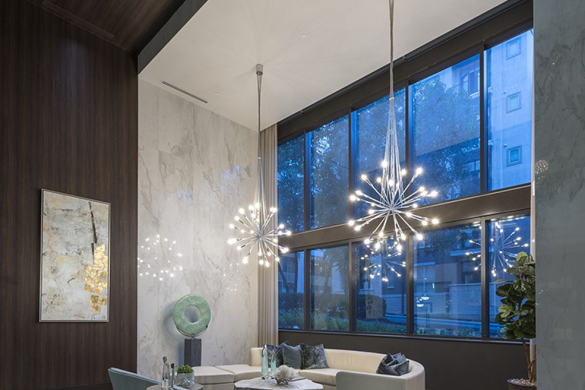 Modern lobby with tall windows, stylish chandeliers, art, and contemporary seating on a patterned rug.