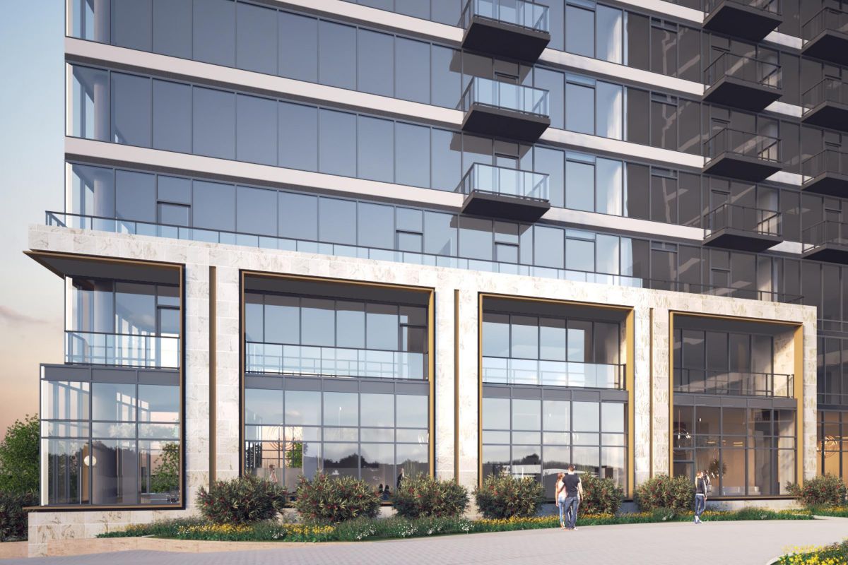 Modern glass building with balconies, ground floor windows, and people walking by on the pavement.
