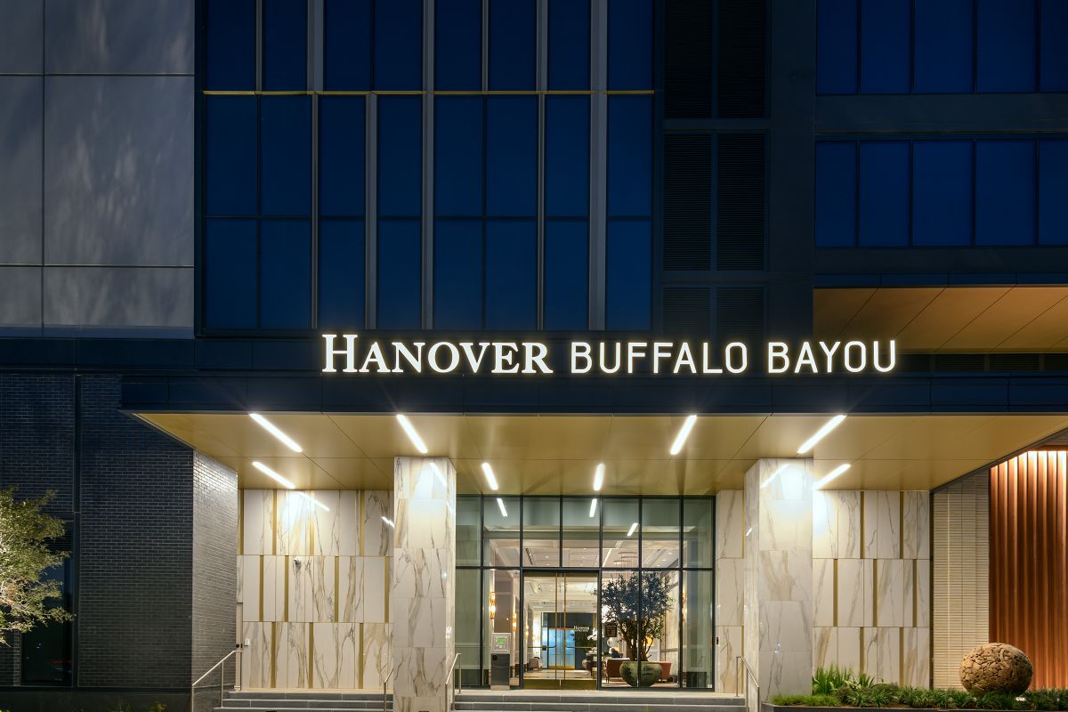 Well-lit modern entrance of Hanover Buffalo Bayou apartments with a glowing sign above the doorway at night.