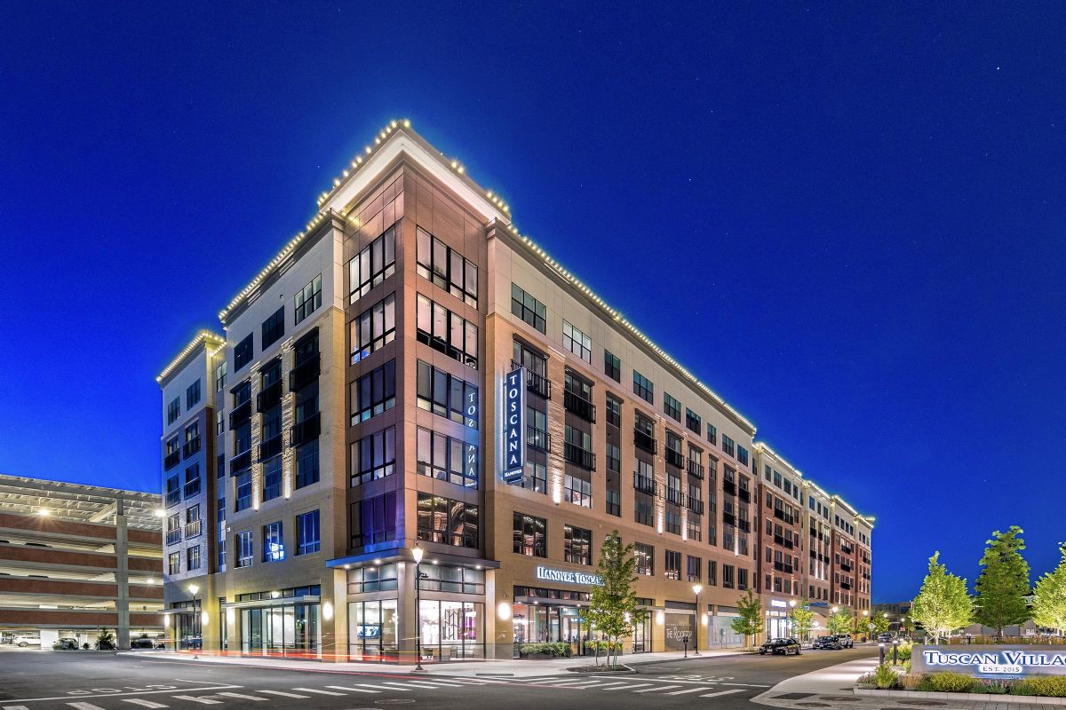 Modern multi-story hotel building with illuminated exterior at night, featuring large windows and a corner entrance.
