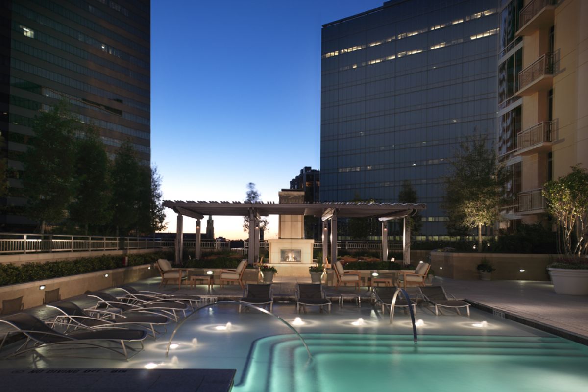 Rooftop pool with lounge chairs and pergola seating area, surrounded by tall office buildings at dusk.