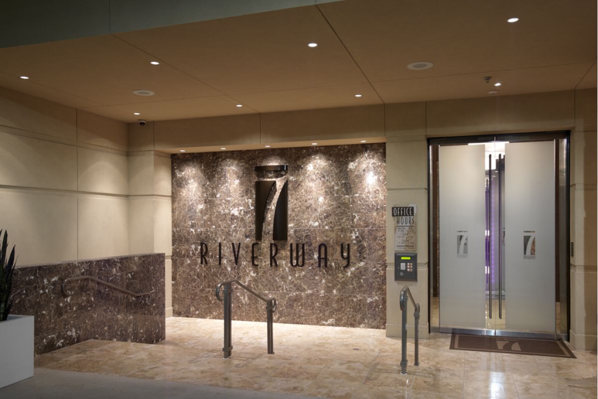 Modern building entrance with "7 Riverway" sign on marble wall and glass doors.
