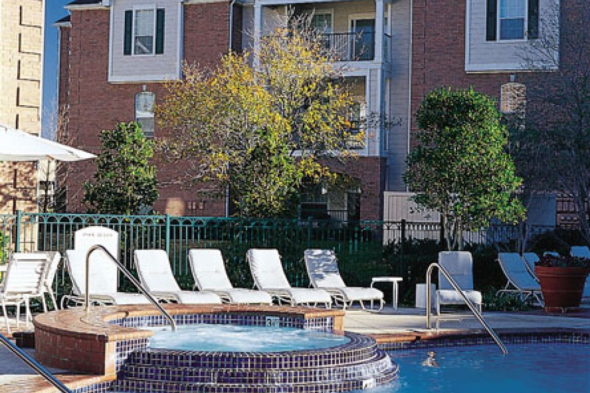 Outdoor pool with lounge chairs, hot tub, and Churchill on the Park’s brick apartment building in the background on a sunny day.